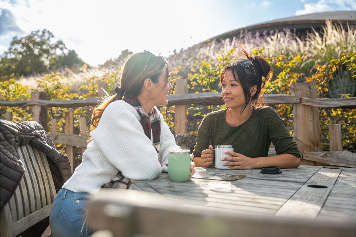 Two people sitting outside on a table, drinking from reusable cups.
