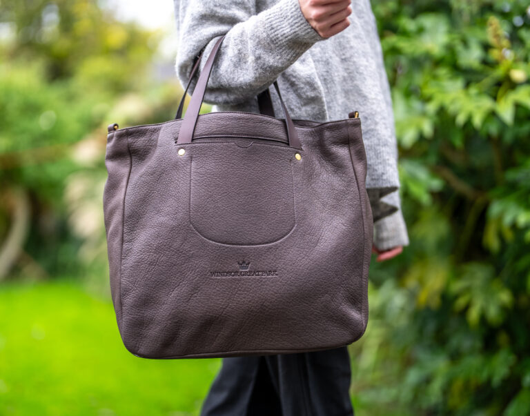An adult holding a dark brown leather bag with a green background.