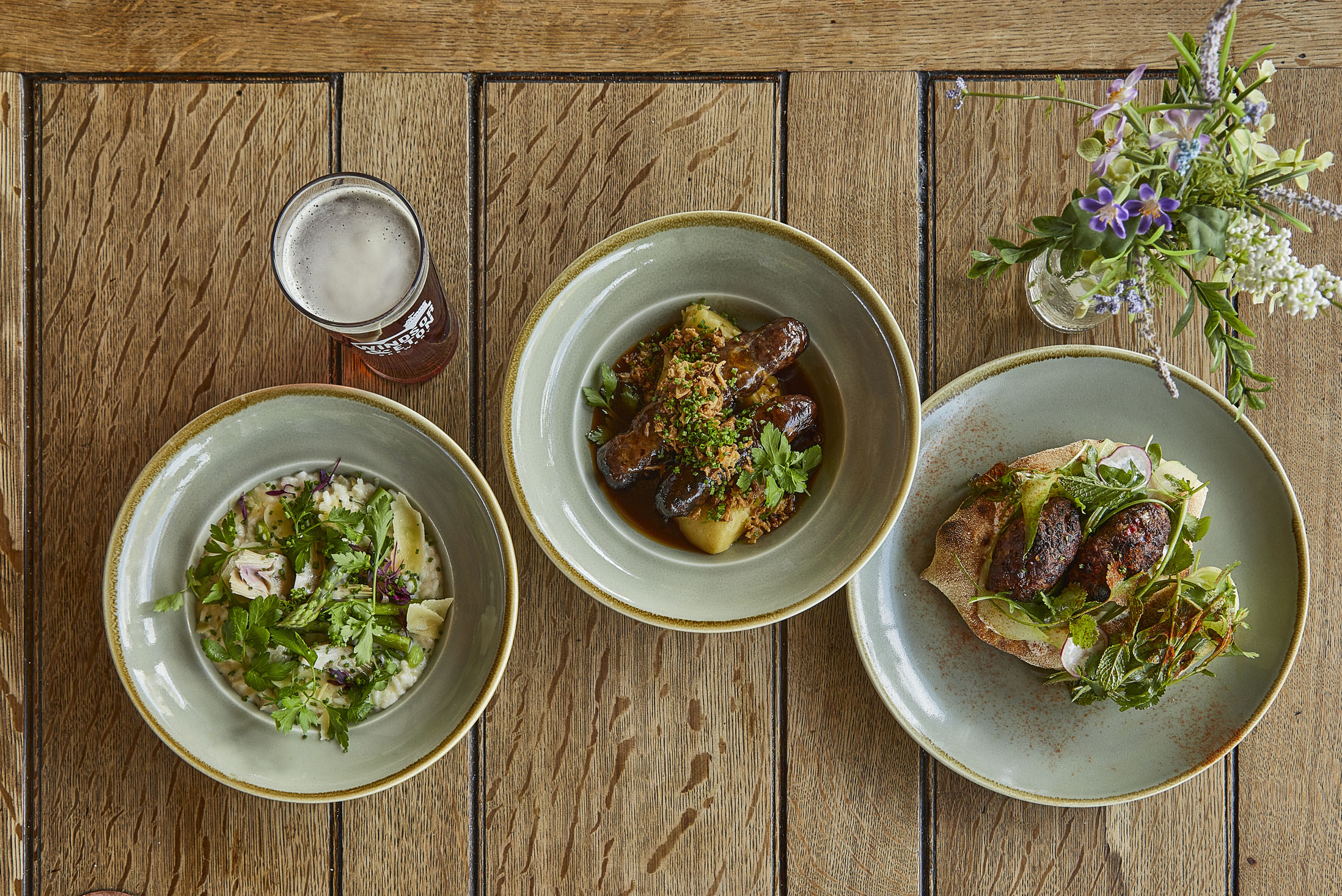 A wooden table with three plates of food and a small floral display.