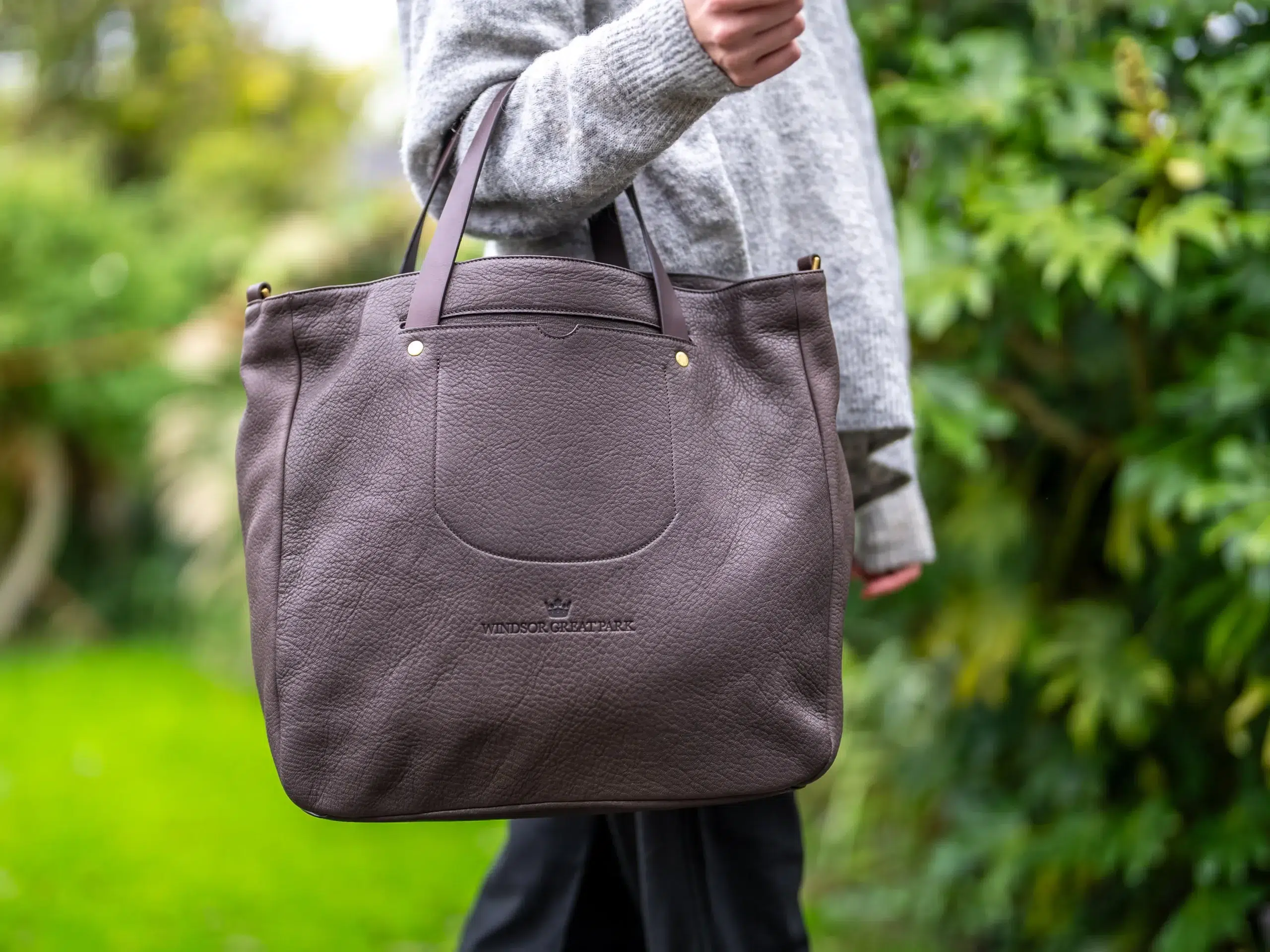 Adult holding a brown leather bag.