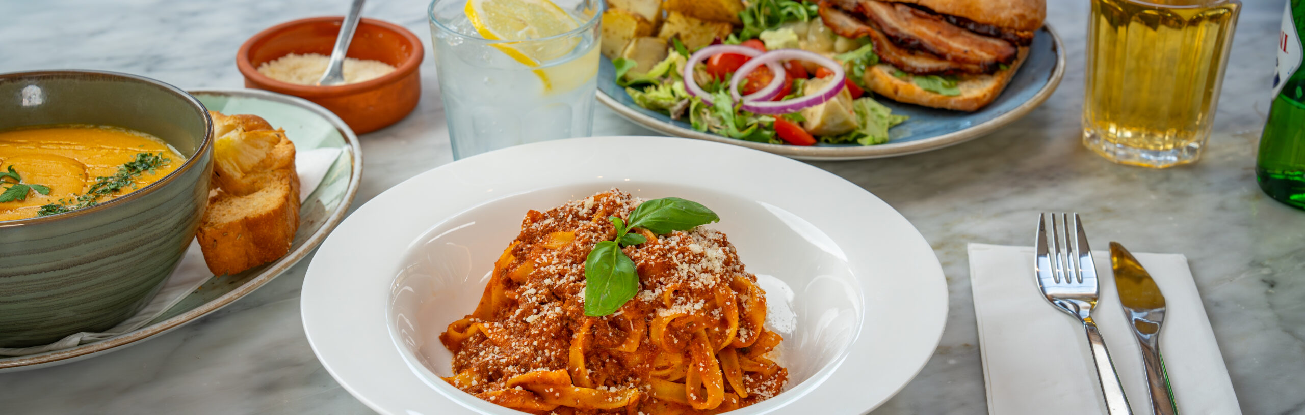 A table laid with a bowl of tagliatelle, soup and cutlery.