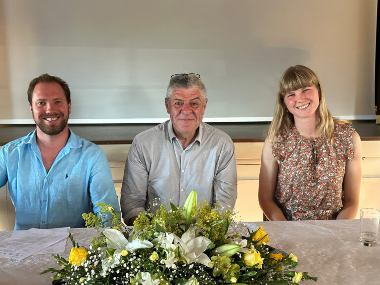 Three people sitting at a table laid with a floral centrepiece.