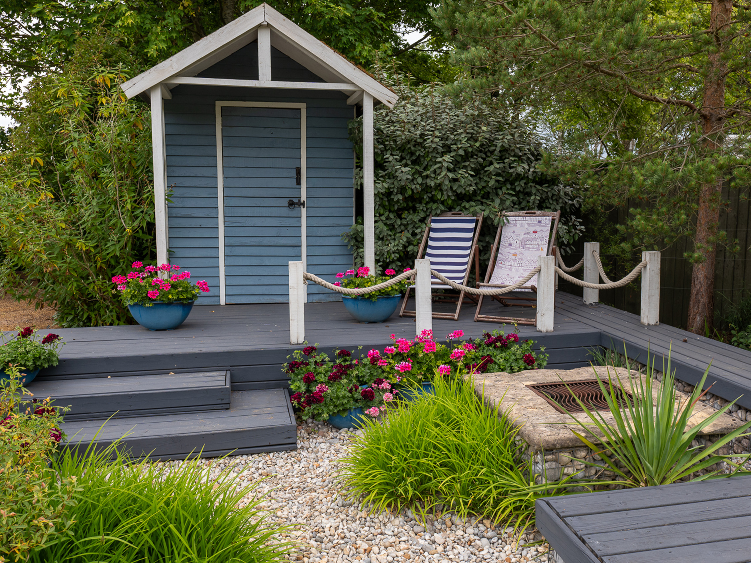 A garden with decking and two deckchairs beside a beach hut.