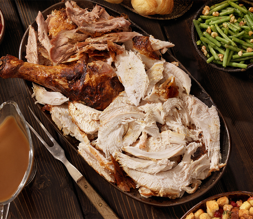 Roast Turkey on a plate of vegetables with candles and other festive trimmings in the background.