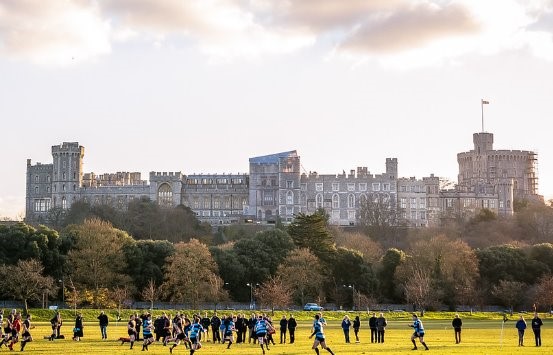 A sports field with people playing football, with Windsor Castle in the distance.