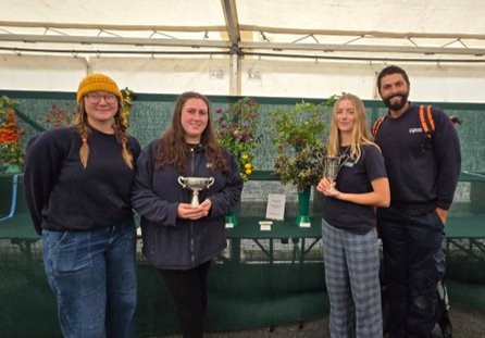 Four people standing in front of a floral display with a trophy.