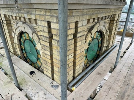 A tower clock face surrounded by scaffolding.