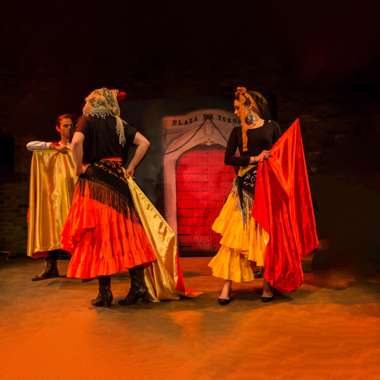 Two adults on stage wearing flamenco type dresses.