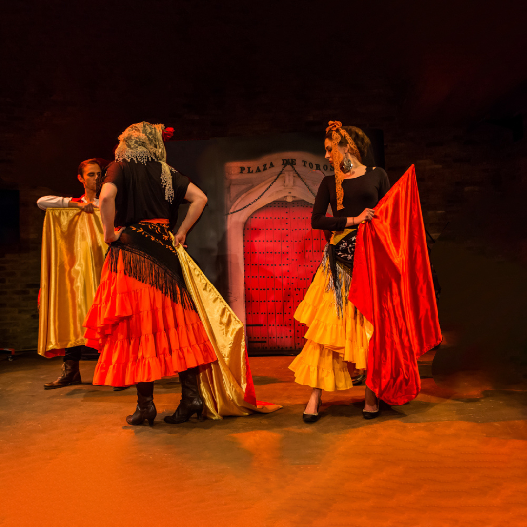 Two adults on stage wearing flamenco type dresses.