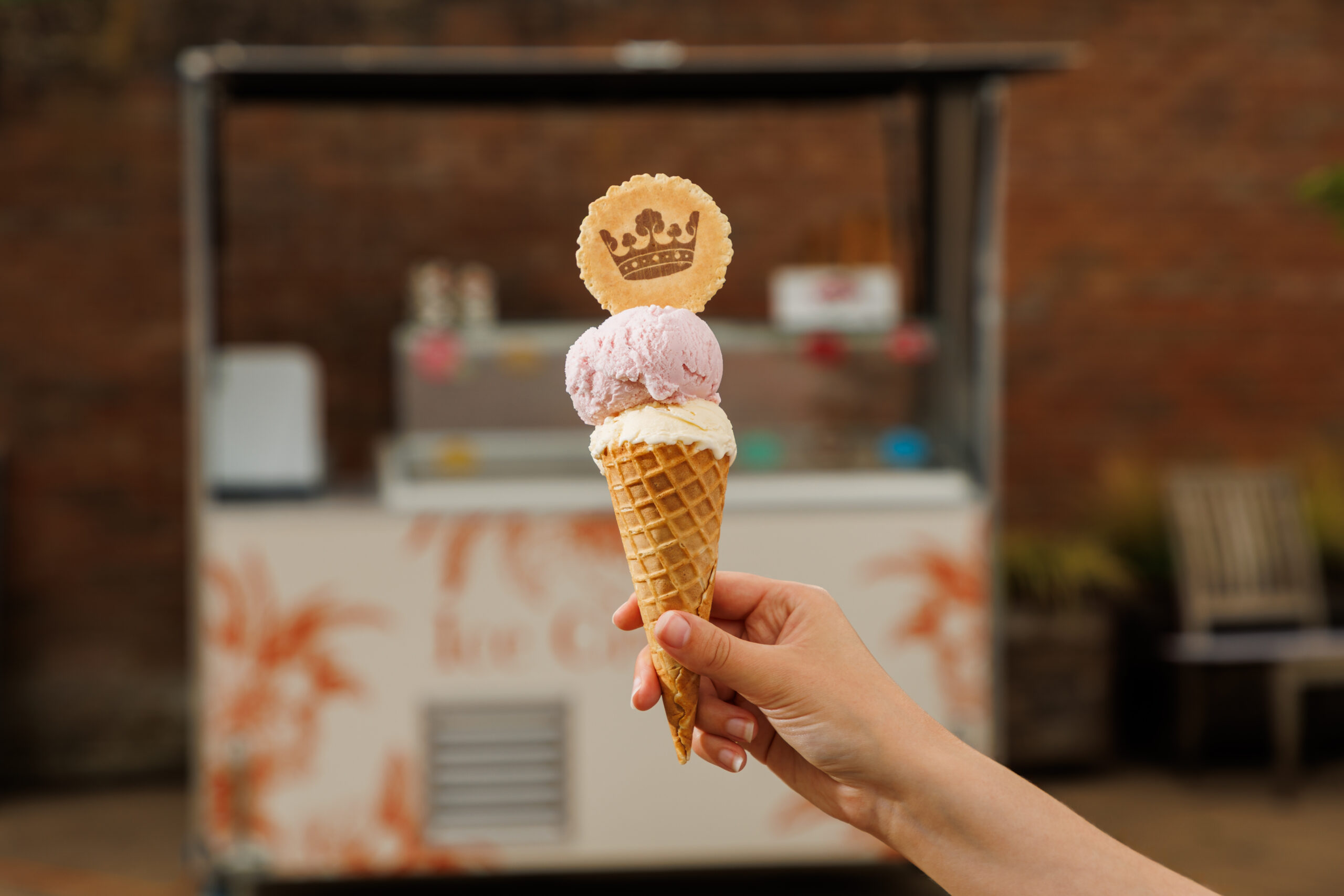 Ice cream cone with a wafer branded with the Windsor Great Park Crown in front of an ice cream cart.