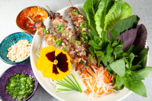 Vietnamese style pork skewers with lettuce leaves and dipping sauce.