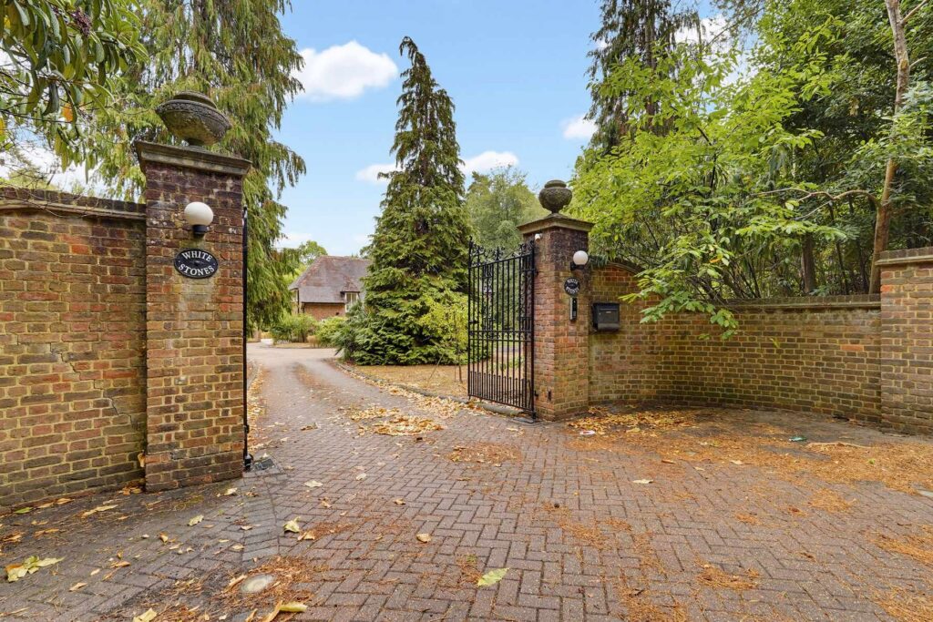 Gated entrance to the property with brick pillars, wrought-iron gates and a long driveway surrounded by mature trees.