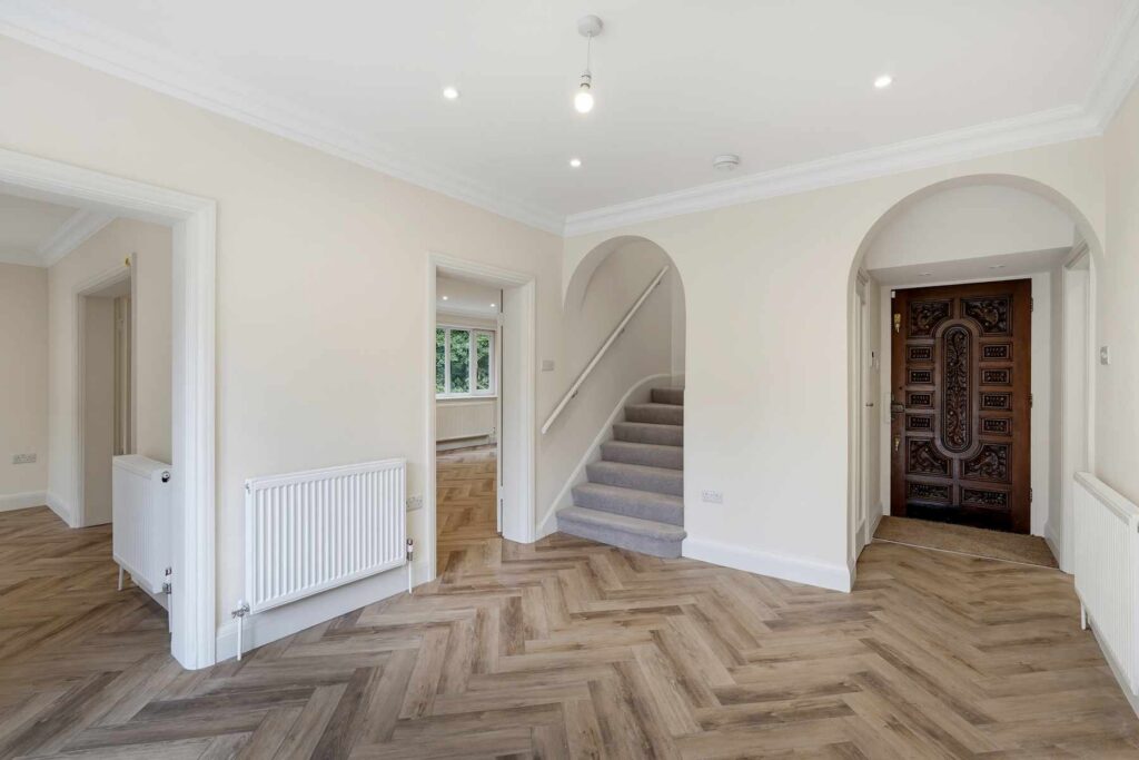 Entrance hallway with herringbone flooring, feature staircase and decorative front door.