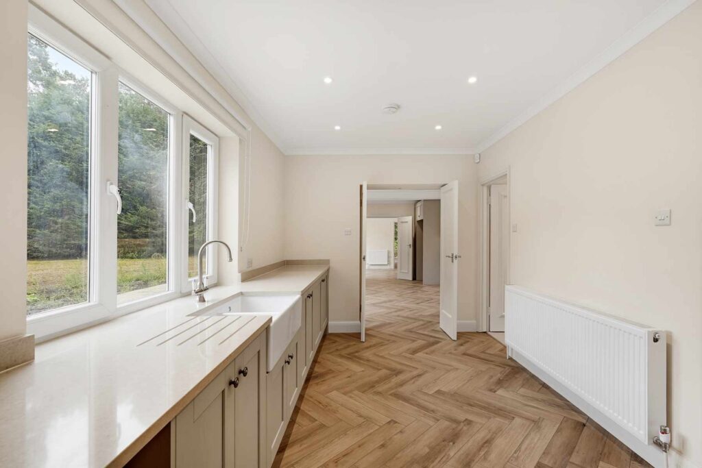 Utility room with farmhouse sink, fitted cupboards and views over the garden.