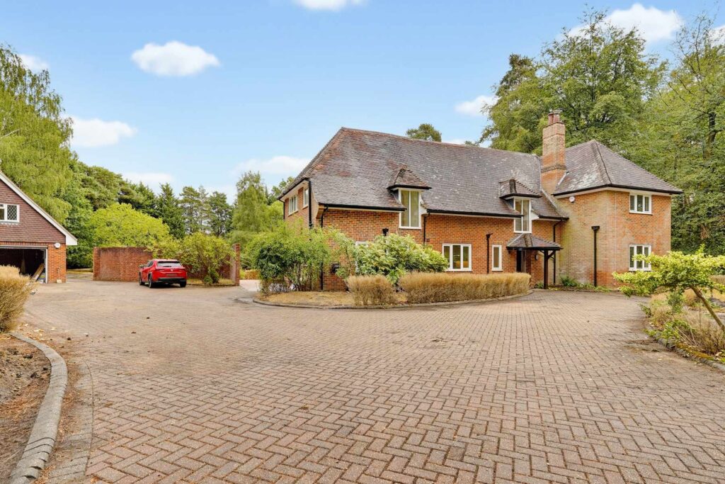 Front elevation of a detached brick house with a large paved driveway, garage and mature landscaping.