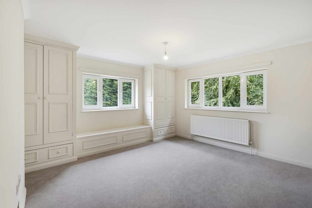 Bright bedroom with fitted wardrobes, built-in window seat and views of surrounding greenery.