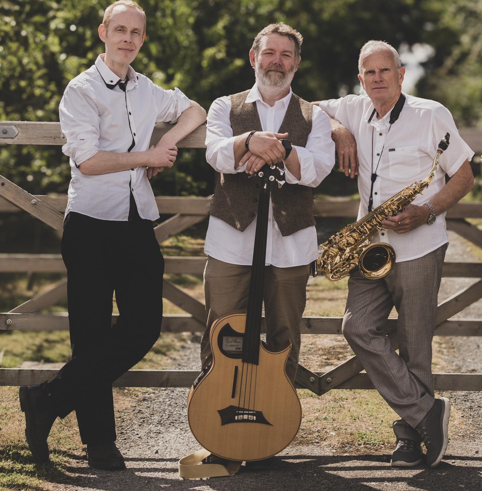 Three people leaning on a fence, holding a guitar and saxophone.