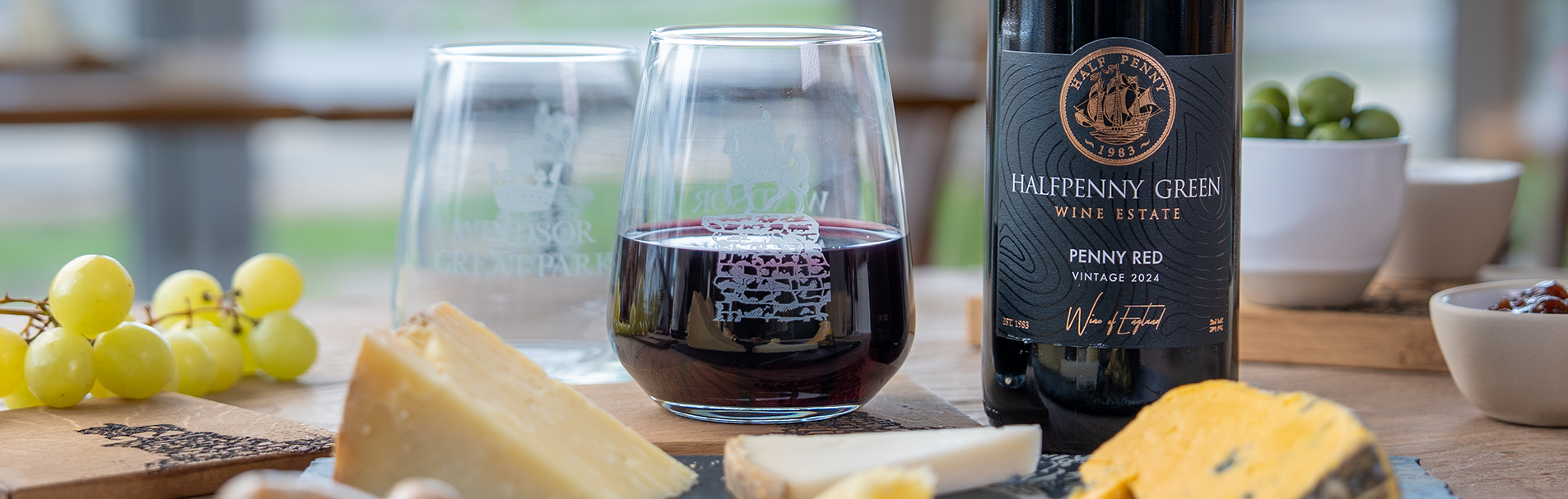 Bottle of red wine with two glasses and a selection of cheeses on a slate board.